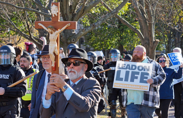 Forced birther in a suit with a large cross